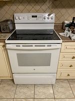Front view of white GE electric range with digital control panel and 5 smooth surface burners.