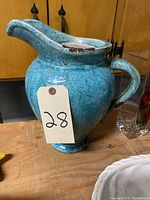 Large blue clay water jug with rustic aged crackled paint finish, visible chips on the rim and worn surface, sitting on a wooden surface.