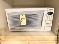 Front view of a white Panasonic inverter microwave oven with control panel on the right and yellow lot tag 54 attached on the door.