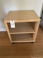 Front view of small wooden printer cabinet showing open front shelf, smooth top surface, and casters.