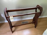 Solid wood clothing rack with heart cutouts on side panels, three horizontal rods, medium brown wood finish, standing on wood floor against a beige wall.