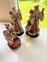 Three Santa figures displayed on table near window, including one music box and two Santa statues.