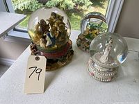 Top view of three decorative water globes arranged on a table near a window, showing the wedding, hummingbirds, and nativity scene globes.