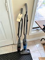 Two stick vacuums standing upright near a door and window, showing overall condition and size comparison.