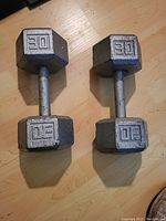 Pair of 30 lb hex dumbbells placed on a wood floor, showing weight markings and overall condition.
