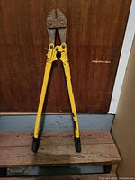 Full view of 36-inch bolt cutters with yellow handles resting against a wooden surface, showing paint wear and black grips on handles.