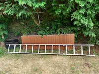 Full view of the aluminum ladder extended and lying on the grass showing the entire length and structure.