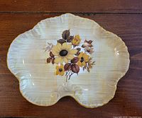 Top view of the leaf-shaped bone china dish with yellow and brown floral design and gold-rimmed edges.