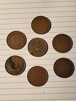 All seven Canadian one cent coins laid out on white lined paper, showing the reverse sides with denomination and years visible.