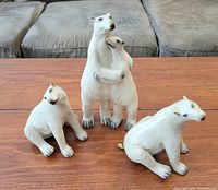 Three ceramic polar bear figurines displayed on wooden surface, largest approx 9 inches tall