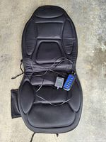 Black padded chair massager laid flat on the ground showing contoured design, remote control, and power adapter.