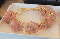 Copper wire bracelet with clusters of pink beads and clear white beads, displayed on white foam inside a white box.