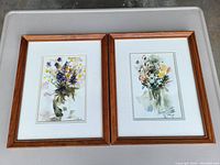 Two framed and matted floral watercolor paintings by Vera McKellar placed side by side on a plastic bin lid, showing overall condition and size.