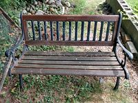 Front view of wooden garden bench showing wooden slats seat and backrest with black metal frame and armrests.