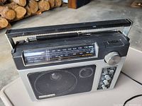 Full view of black and silver General Electric Superadio vintage portable radio with handle, tuning dial, speaker, and buttons visible on the front.
