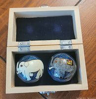 Two harmony balls with elephant designs in an open light wood box with black interior.