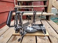 Manual mitre saw mounted on a metal adjustable stand with angle guides, placed on wooden steps outdoors.