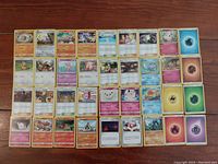Top-down photo showing 36 Pokemon cards laid out on a wooden surface. Cards include Pokemon characters, Trainer cards, and Energy cards mainly from 2019 with two from 2007.