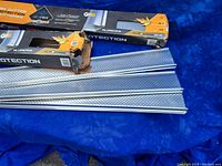 Two damaged boxes containing metal rain gutter protectors, with some protectors removed and displayed. The protectors are perforated metal strips approximately 3 feet in length.