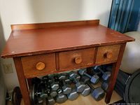 Wooden desk/table with three front drawers, showing the full front view with drawers closed.
