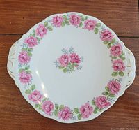 Top view of bone china cake plate showing pink rose pattern on white background with small handles and gold accents.
