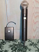 Wireless handheld Shure SM58 microphone standing upright next to a wireless receiver pack.