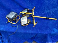Photo showing two work lights on a yellow frame stand and one separate light on blue background