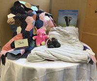 Photo showing the full lot with quilt, pink elephant plush toy, baby sleep sac with stripes and elephant embroidery, black baby shoes, and the elephant book.