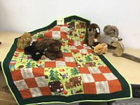Quilt folded with 7 stuffed animals on top, showing wildlife quilt pattern and plush animals