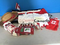 Photo showing crocheted afghan, Canadian-themed men's t-shirts, small Canadian flag, woven hat, slipper socks, and other Canadian accessories on table against blue background