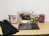 Lot contents including marble pastry board, three recipe books, black trivet, and black chef's apron