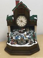 Front view of the clock showing the house shape, clock face, and snowy village scene.