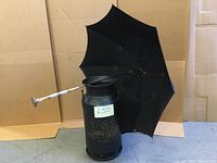 Black decorative antique milk can with floral design and black umbrella with mother of pearl and brass handle leaning against it.