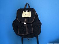 Front view of black Fossil backpack with flap buckle closure and front pocket against blue background.