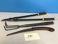 Overall view of three garden tools including a long-handled clipper/pruner, a 3-prong hand cultivator, and a curved saw-like tool with wooden handle.