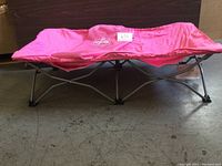 Full view of the pink Regalo folding cot with metal frame on the floor showing the extended legs and fabric surface.