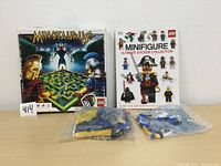 Lego Minotaurus game box, Minifigure Ultimate Sticker Collection book, and two sealed bags of Lego pieces on a white surface.