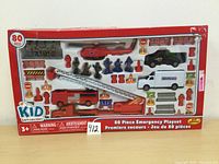 Front of box showing included figurines and vehicles arranged in tray, highlighting fire truck, helicopter, and emergency personnel figures.