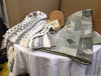 Photo of taupe quilt folded showing leaf pattern and knit throw blanket on top with wooden quilt hanger behind