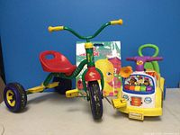 Kiddi-o tricycle, Fisher-Price Little People riding toy, and Jumbo Grande coloring book displayed against blue background.