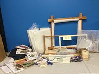 Image showing wooden embroidery frames, white fabric pieces, plastic canvas sheets and cord materials displayed on a flat surface against blue wall