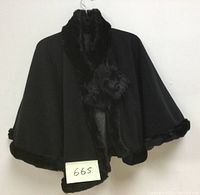Black women’s short cape hanging, showing faux fur trim along collar and edges.