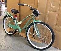 Full side view of light green women’s Super Cycle Classic cruiser bicycle with whitewall tires, rear rack, fenders, and coil lock on seat post.