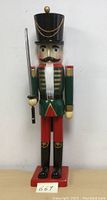 Front view showing painted face, green coat with gold trim, red pants, black boots, black top hat with gold chains and held sword