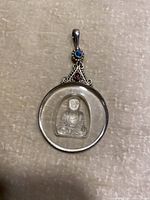 Front view of the pendant showing the crystal Buddha inside a circular silver frame with blue and red stones.