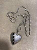 Sterling silver necklace with heart-shaped pendant featuring five small black stones, displayed on beige background.