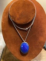 Silver necklace displayed on a rust-colored jewelry stand with the lapis lazuli pendant centered, showing chain and pendant details.