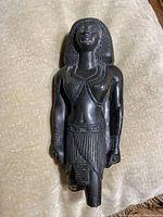 Front view of an antique Egyptian-style black stone statue showing detailed face, traditional clothing, and jewelry.