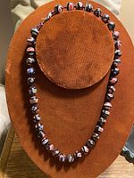 Full view of antique millefiori necklace showing arrangement of black beads with multicolored floral patterns on orange fabric display.