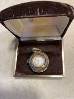 Antique eye-shaped pendant watch in presentation box showing front and top angles.